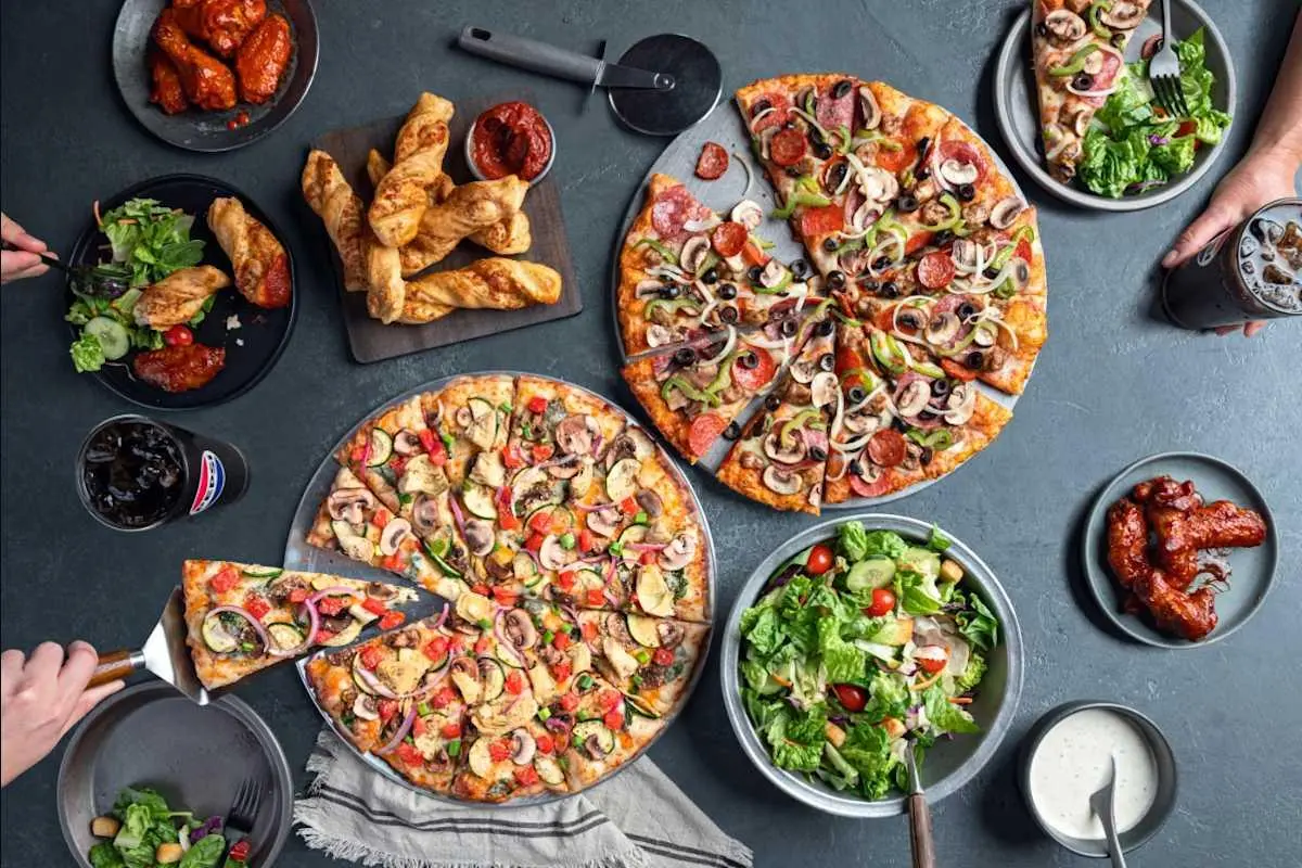 Large spread of pizzas, wings, and sides highlighting Pizza Hut delivery deals.